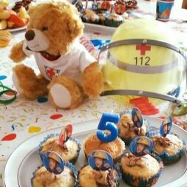 DRK-Kindergeburtstag Muffins mit einer 5 sind auf einer Geburtstagsdecke angerichtet, ein DRK-Helm und ein Trösteteddy daneben